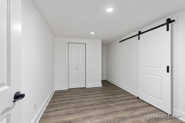 unfurnished bedroom with a barn door, a closet, and dark hardwood / wood-style floors