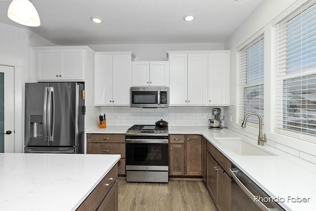 kitchen featuring pendant lighting, sink, decorative backsplash, white cabinetry, and stainless steel appliances