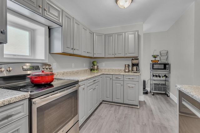 kitchen with light stone countertops, stainless steel appliances, light hardwood / wood-style flooring, and gray cabinetry