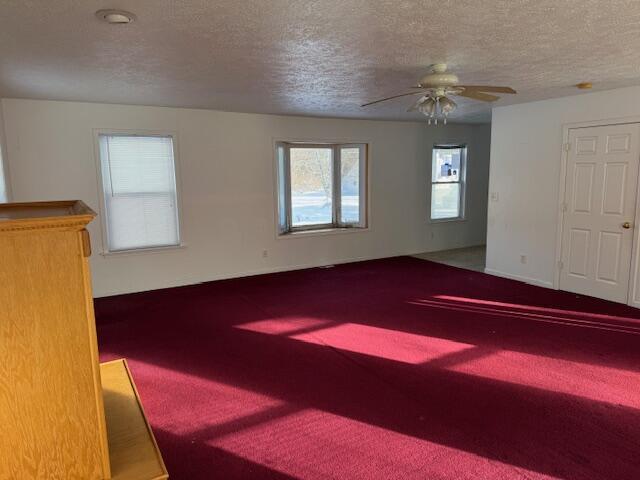 carpeted empty room with ceiling fan and a textured ceiling