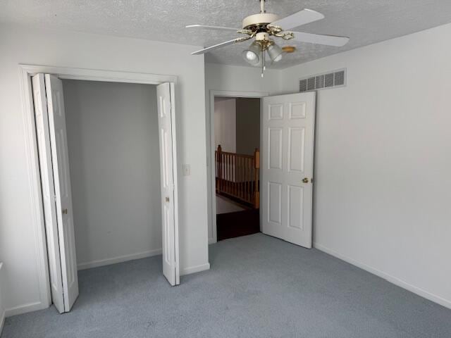 unfurnished bedroom featuring a textured ceiling, a closet, ceiling fan, and light colored carpet