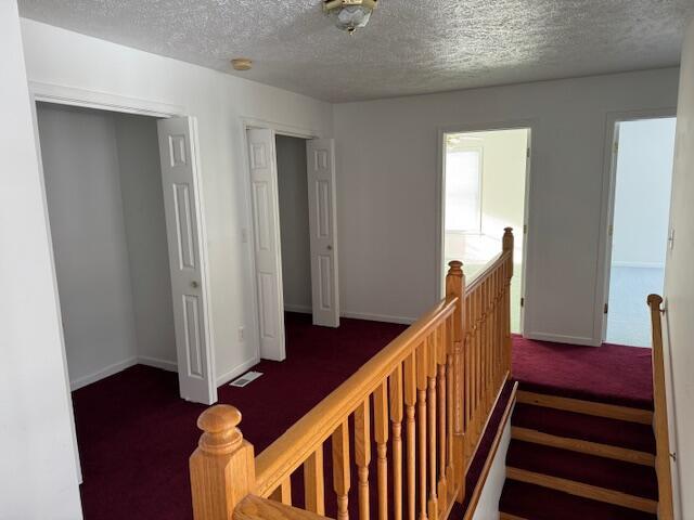 hall featuring dark carpet and a textured ceiling