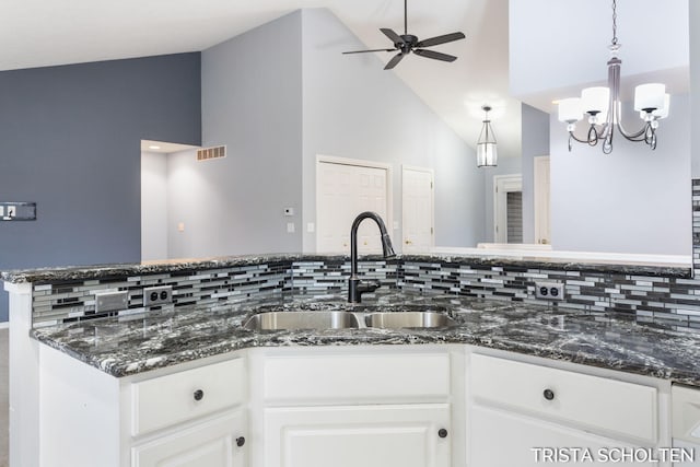 kitchen with white cabinetry, sink, tasteful backsplash, dark stone countertops, and ceiling fan with notable chandelier