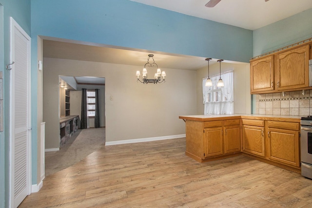 kitchen featuring decorative light fixtures, light wood-type flooring, kitchen peninsula, and stainless steel stove