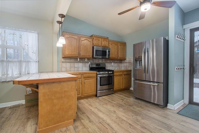 kitchen featuring tile counters, light wood-type flooring, stainless steel appliances, and hanging light fixtures