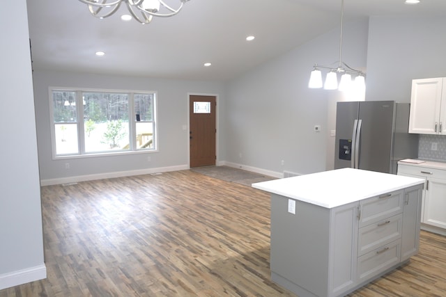 kitchen with vaulted ceiling, a chandelier, stainless steel fridge with ice dispenser, tasteful backsplash, and a kitchen island