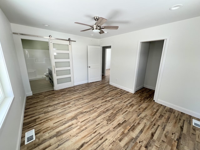 unfurnished bedroom featuring ceiling fan, connected bathroom, a barn door, and hardwood / wood-style flooring