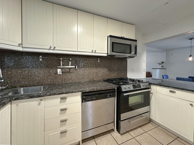 kitchen with sink, stainless steel appliances, dark stone countertops, decorative backsplash, and light tile patterned floors