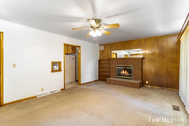 unfurnished living room featuring ceiling fan, wood walls, light colored carpet, and a fireplace