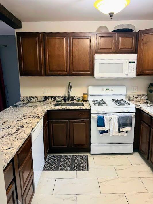 kitchen with dark brown cabinets, light stone countertops, white appliances, and sink