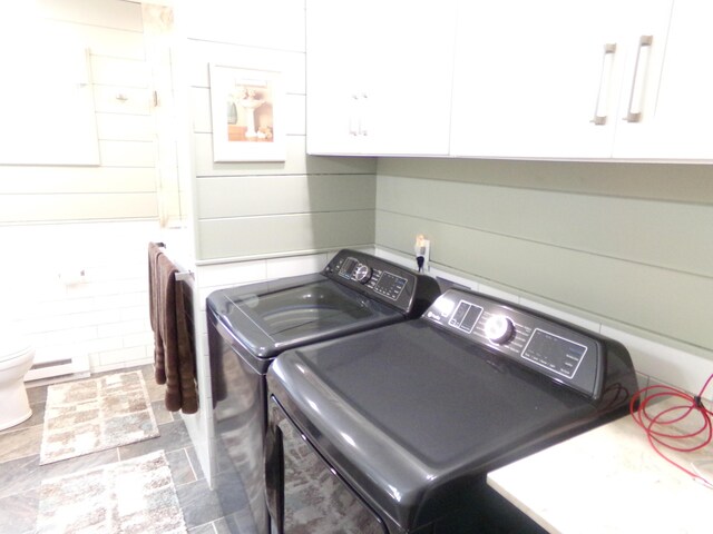 clothes washing area featuring independent washer and dryer, wooden walls, and a baseboard radiator