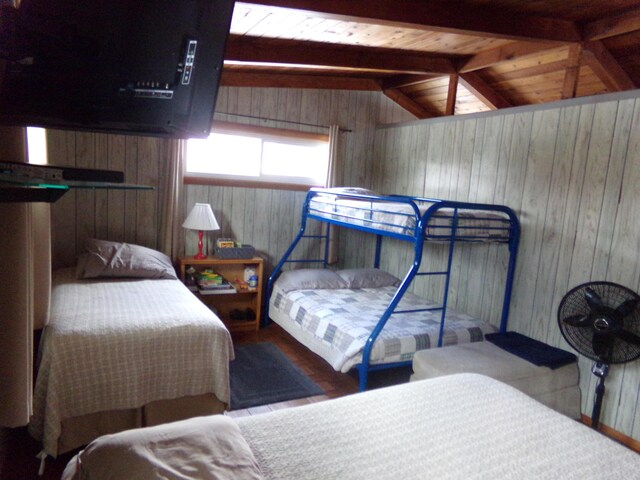 bedroom with wood walls, vaulted ceiling with beams, and wood ceiling