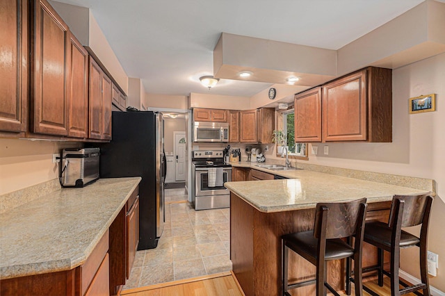 kitchen with a kitchen breakfast bar, sink, light hardwood / wood-style floors, kitchen peninsula, and stainless steel appliances