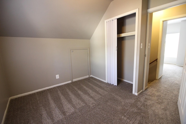 unfurnished bedroom with a closet, lofted ceiling, and dark colored carpet