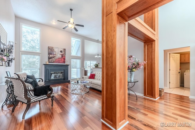 living room featuring light wood-type flooring, washer / dryer, a wealth of natural light, a high ceiling, and ceiling fan with notable chandelier