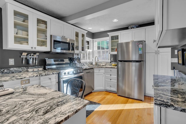 kitchen featuring a textured ceiling, stainless steel appliances, stone counters, white cabinets, and light hardwood / wood-style floors