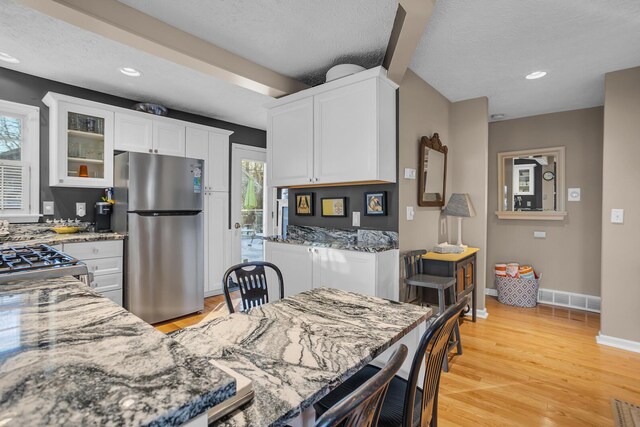 kitchen with appliances with stainless steel finishes, light wood-type flooring, dark stone counters, a textured ceiling, and white cabinetry