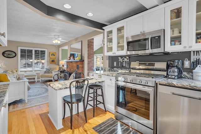 kitchen featuring white cabinets, light stone countertops, appliances with stainless steel finishes, light hardwood / wood-style floors, and kitchen peninsula