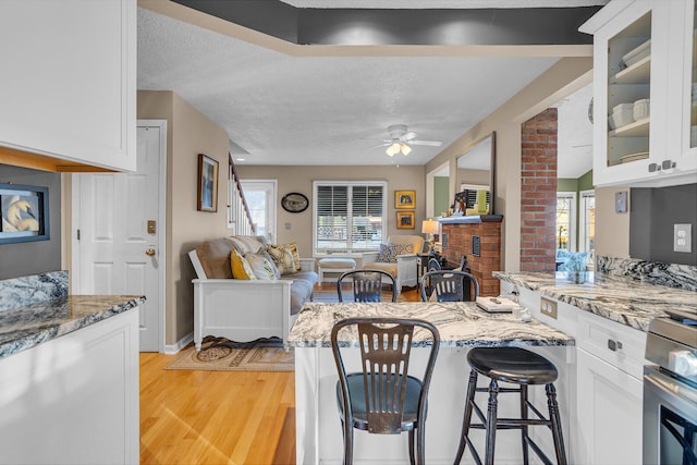 kitchen featuring white cabinets, a textured ceiling, stainless steel range, light hardwood / wood-style floors, and light stone counters