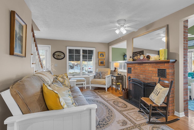 living room featuring a fireplace, light hardwood / wood-style floors, a textured ceiling, and ceiling fan