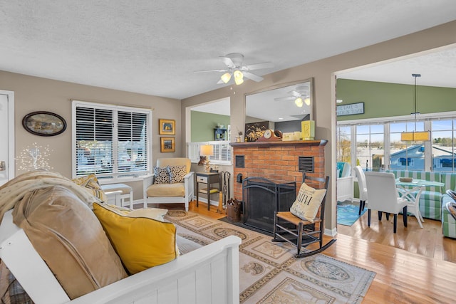 living room with a brick fireplace, a textured ceiling, ceiling fan, light hardwood / wood-style floors, and lofted ceiling