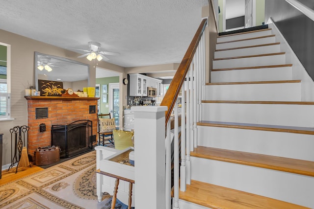 stairway with a textured ceiling, ceiling fan, a fireplace, and a wealth of natural light