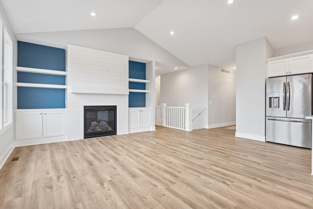 unfurnished living room featuring built in shelves, vaulted ceiling, a fireplace, and light hardwood / wood-style flooring