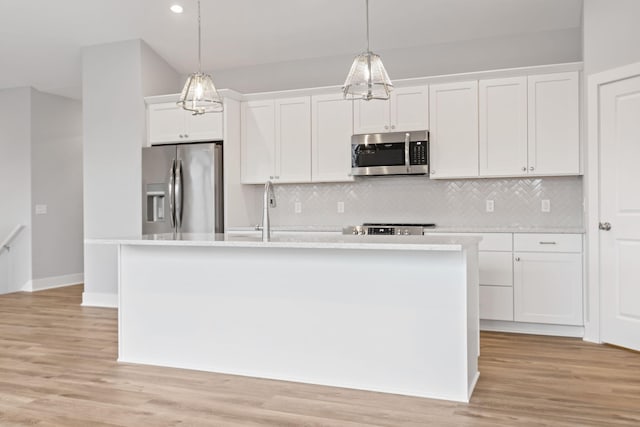 kitchen featuring a center island with sink, hanging light fixtures, appliances with stainless steel finishes, tasteful backsplash, and white cabinetry