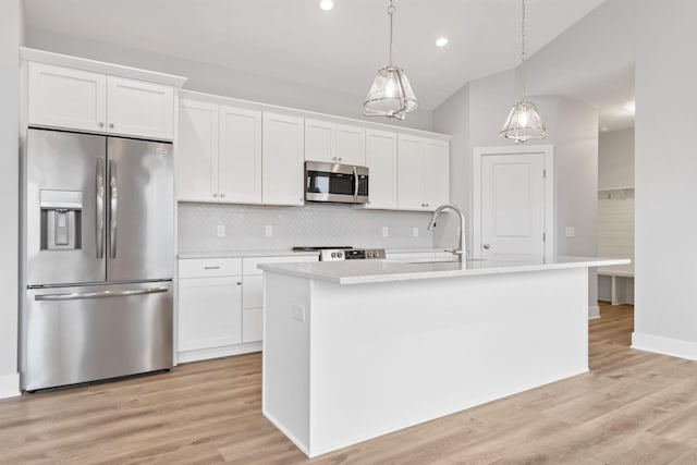 kitchen with appliances with stainless steel finishes, decorative light fixtures, white cabinetry, and a kitchen island with sink