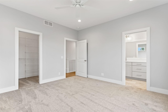 unfurnished bedroom featuring ceiling fan, ensuite bathroom, light colored carpet, and a spacious closet