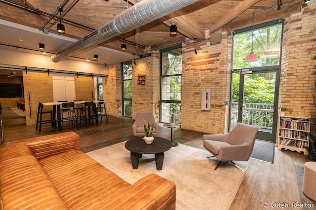 living room with a barn door, a towering ceiling, brick wall, and hardwood / wood-style flooring