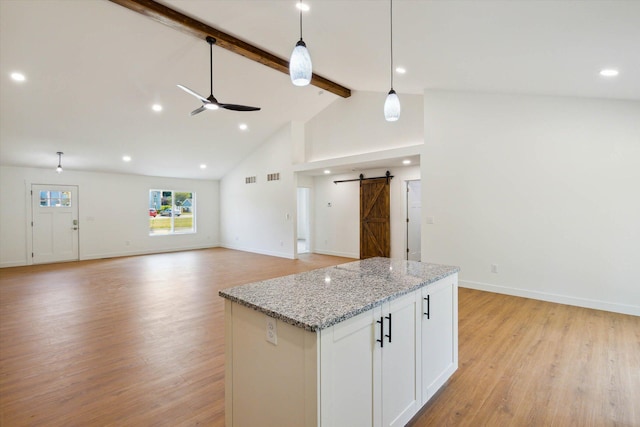 kitchen featuring white cabinetry, a barn door, light hardwood / wood-style flooring, beamed ceiling, and pendant lighting