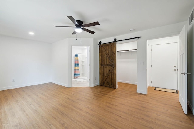 unfurnished bedroom featuring ceiling fan, a barn door, connected bathroom, light hardwood / wood-style floors, and a closet