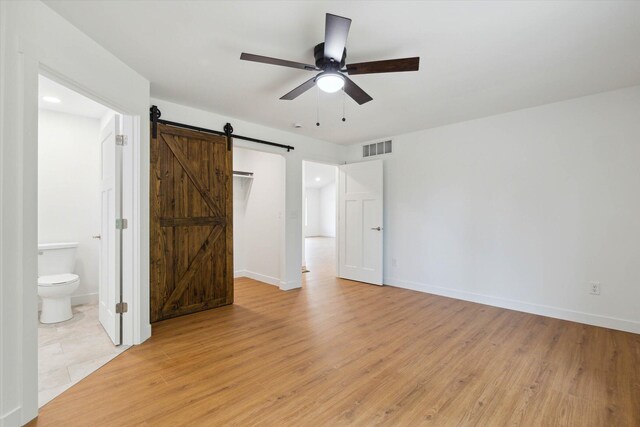 unfurnished bedroom featuring a barn door, ceiling fan, light hardwood / wood-style flooring, and ensuite bath