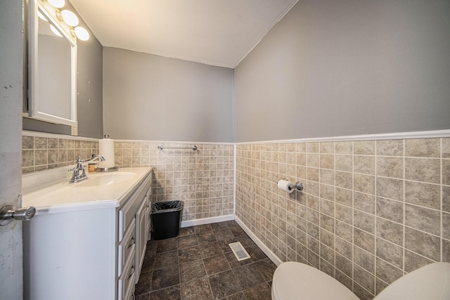 bathroom featuring vanity, toilet, and tile walls