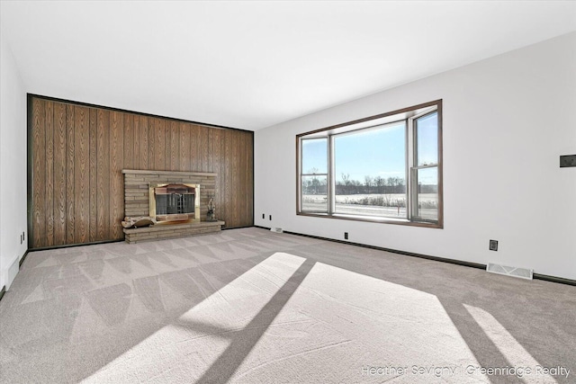 unfurnished living room with light carpet, a stone fireplace, and wooden walls