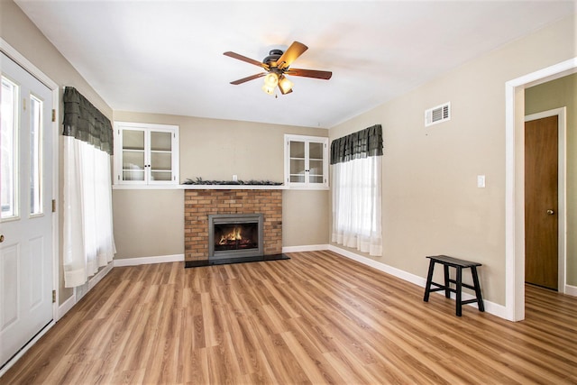 unfurnished living room with a brick fireplace, ceiling fan, and light wood-type flooring