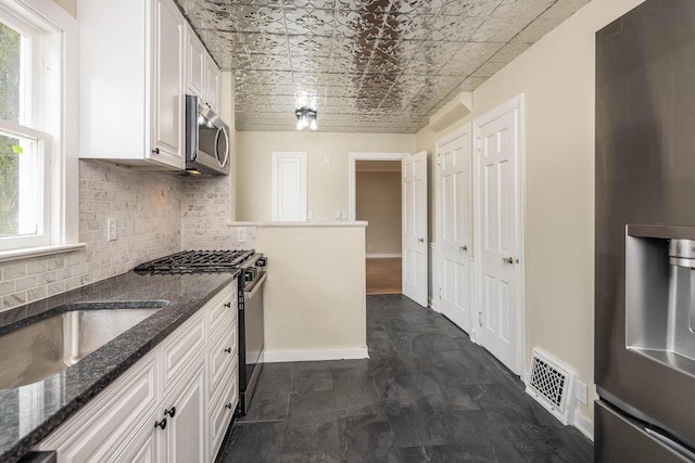 kitchen with stainless steel appliances, white cabinetry, tasteful backsplash, and dark stone countertops