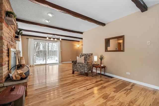 living area featuring beamed ceiling, a textured ceiling, light hardwood / wood-style floors, and a fireplace