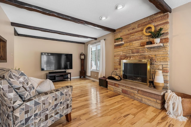 living room with a textured ceiling, beam ceiling, a fireplace, and light hardwood / wood-style flooring