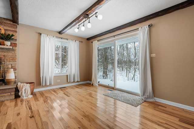 doorway to outside with beam ceiling, a textured ceiling, and light wood-type flooring