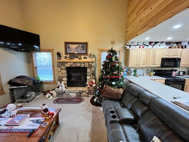 living room with carpet flooring, a stone fireplace, and a towering ceiling