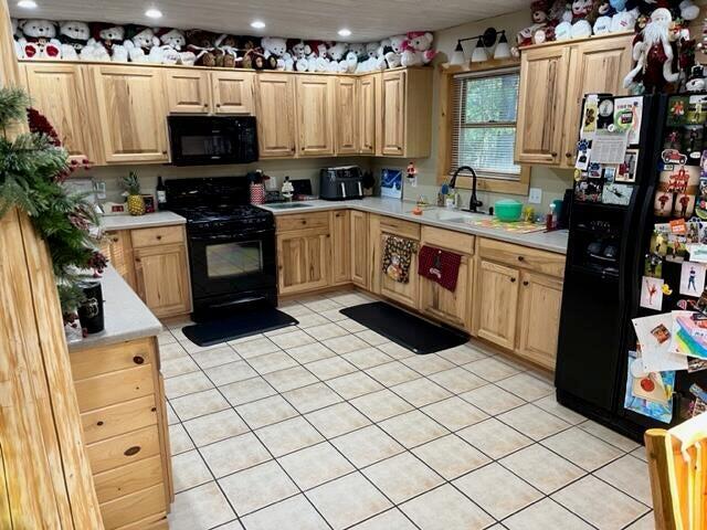 kitchen with light brown cabinetry, light tile patterned floors, black appliances, and sink