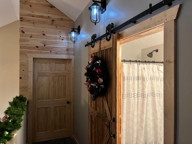 interior space with wood walls, a barn door, and vaulted ceiling