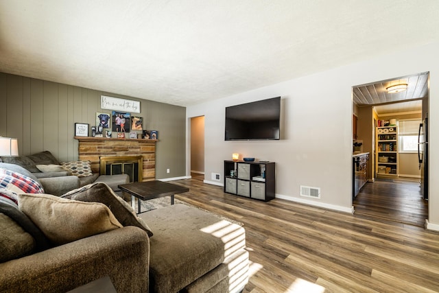 living room featuring hardwood / wood-style floors, wood walls, a stone fireplace, and a textured ceiling