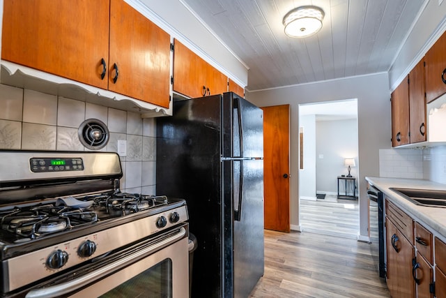 kitchen featuring black refrigerator, tasteful backsplash, gas stove, crown molding, and light hardwood / wood-style flooring