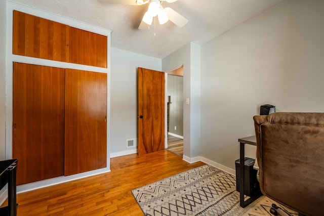 living area with ceiling fan, light hardwood / wood-style floors, and a textured ceiling