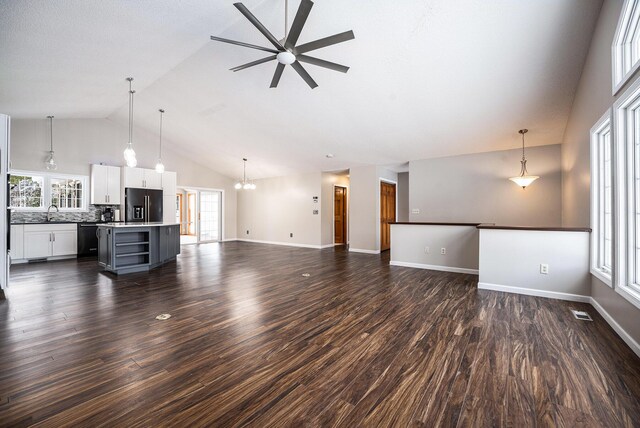 unfurnished living room with ceiling fan with notable chandelier, dark hardwood / wood-style floors, sink, and vaulted ceiling