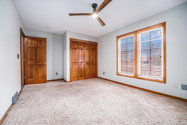 unfurnished bedroom featuring ceiling fan, a closet, light colored carpet, and a textured ceiling