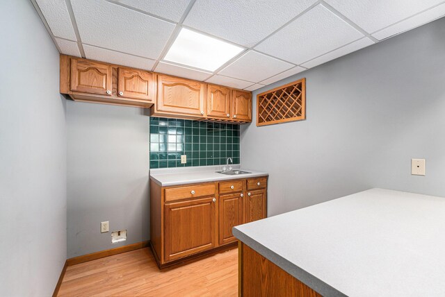 kitchen featuring backsplash, a drop ceiling, sink, and light hardwood / wood-style flooring